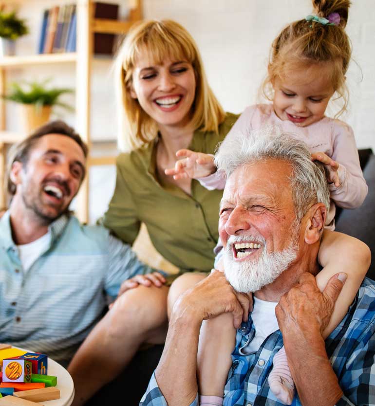 Happy senior man surrounded by his family, including a woman, a man, and a young child playing.