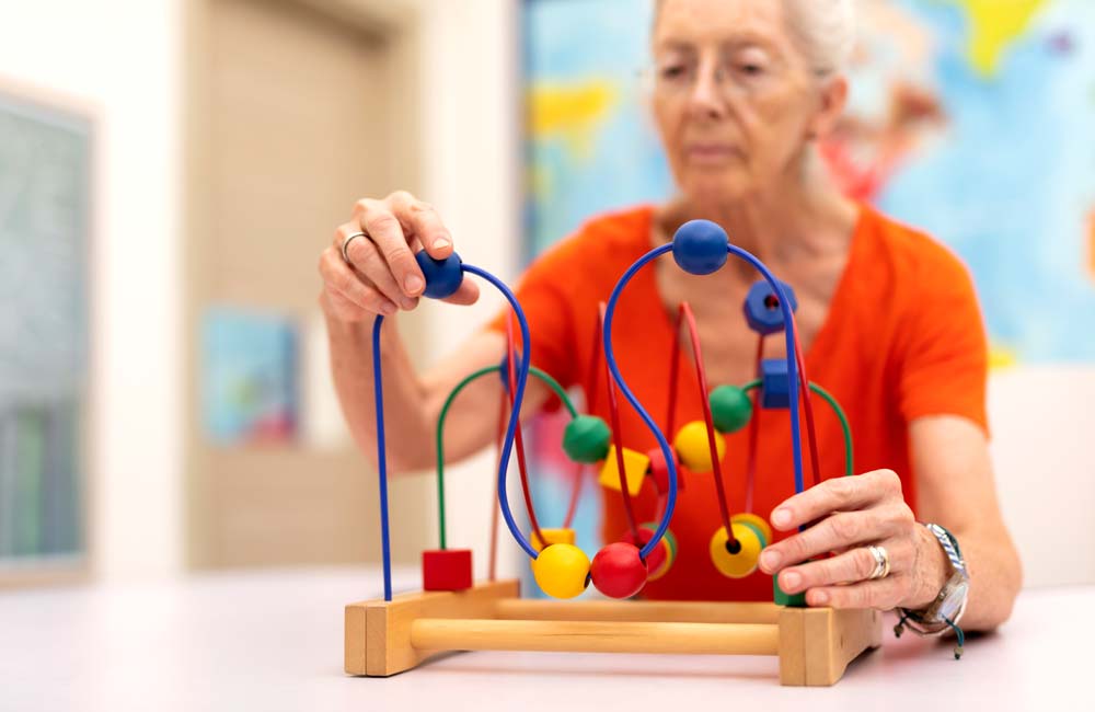 Senior woman in orange shirt engaged in memory care activity using a colorful bead maze.